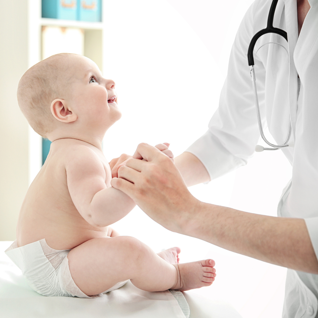 Ein Baby sitzt auf dem Tisch des Arztes und lächelt den Arzt an, der seine Hand hält.