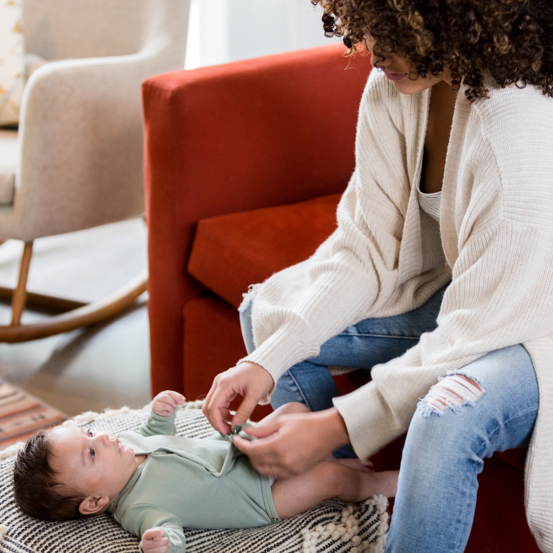 baby richtig anziehen: Eine lächelnde Mutter schließt die Knöpfe an der Kleidung ihres Babys