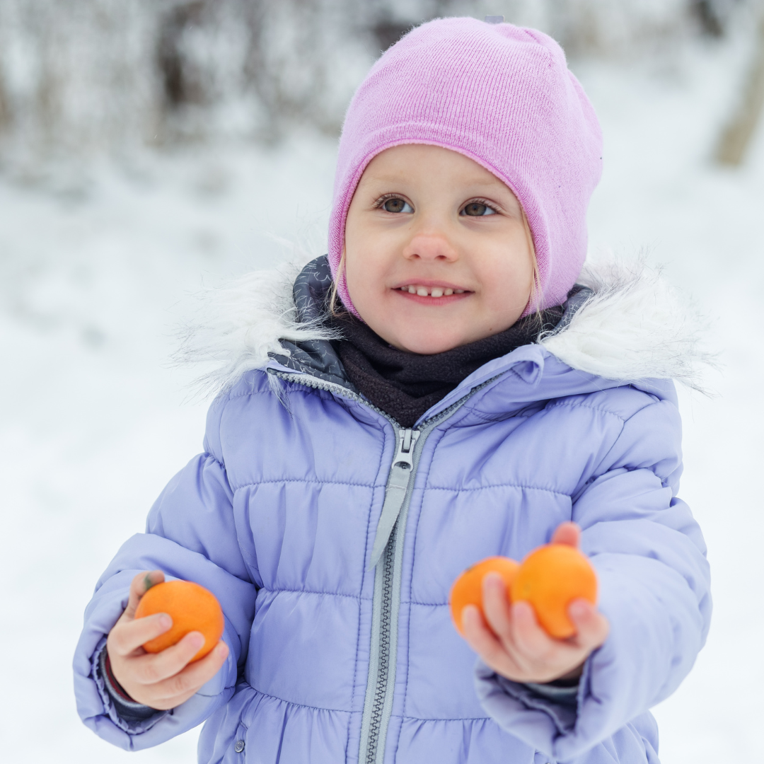 a child holding oranges in the snow