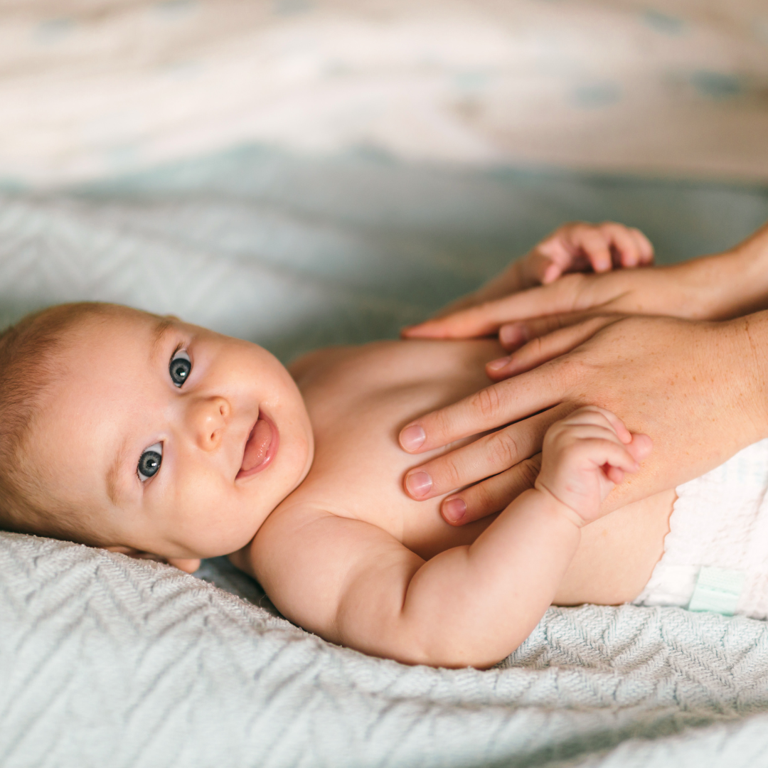 Baby liegt auf dem Bett und wird sanft massiert 